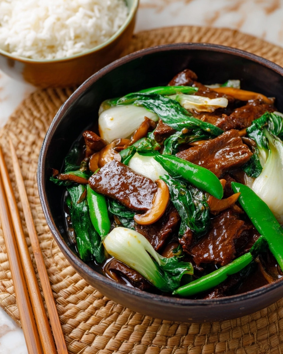The dish shows a dark bowl filled with a stir-fry that has vibrant layers: at the base are thick, glossy pieces of brown cooked meat covered partially with a shiny dark brown sauce. Scattered throughout are bright green snap peas and dark green wilted leafy greens, adding fresh color. There are also smooth white chunks of bok choy and light brown mushrooms that bring in varied textures. The bowl sits on a tan woven mat on top of a white marbled surface, with a pair of wooden chopsticks beside it and a white bowl of steamed rice partially visible at the top. photo taken with an iphone --ar 4:5 --v 7