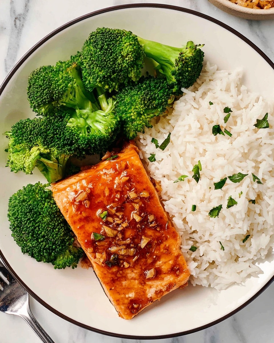 A white plate with a thin black rim holds three main layers arranged side by side: on the left, bright green broccoli florets with detailed texture showing small buds and stalks; in the middle, a square piece of cooked salmon covered with a shiny, reddish-brown glaze and small bits of garlic and chopped herbs on top; on the right, a bed of fluffy white rice with slightly separated grains underneath and spilling to the edge of the plate. The plate sits on a white marbled surface, with a silver fork partially visible at the lower left corner. Photo taken with an iphone --ar 4:5 --v 7