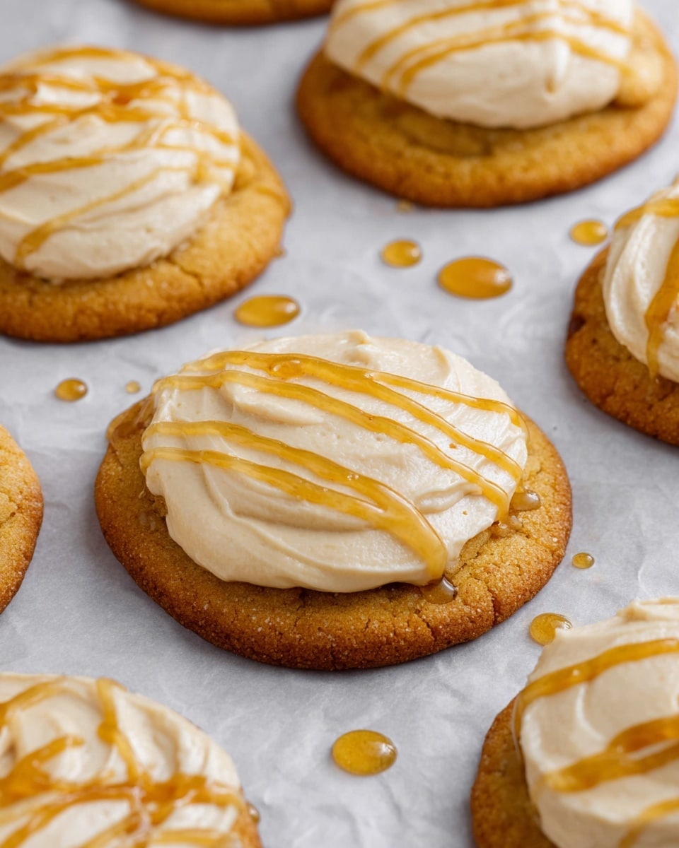 The image shows several round cookies placed on white parchment paper over a white marbled surface. Each cookie has two layers: the bottom layer is golden brown and slightly textured, while the top layer is a thick spread of creamy light beige frosting, with a smooth and slightly swirled texture. On top of the frosting, there are thin, shiny, golden drizzles of honey that catch the light, creating a warm contrast against the frosting. Some honey droplets are also scattered on the parchment next to the cookies, adding extra shine and a sticky look. Photo taken with an iphone --ar 4:5 --v 7