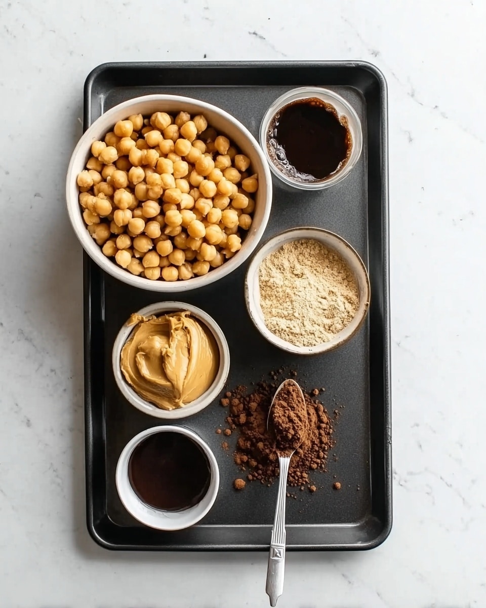 The image shows a black baking tray on a white marbled surface holding five small white bowls with different ingredients. The largest bowl, placed on the upper left side, is filled with round, light brown chickpeas. To its upper right, a small bowl contains dark brown thick liquid, next to which is another bowl filled with a light beige powdery substance. Below, on the left side, there is a bowl with creamy golden peanut butter, and in front of it, a very small bowl holds dark brown liquid. Lastly, on the right side, there is a metal spoon filled with fine dark brown powder. The photo taken with an iphone --ar 4:5 --v 7