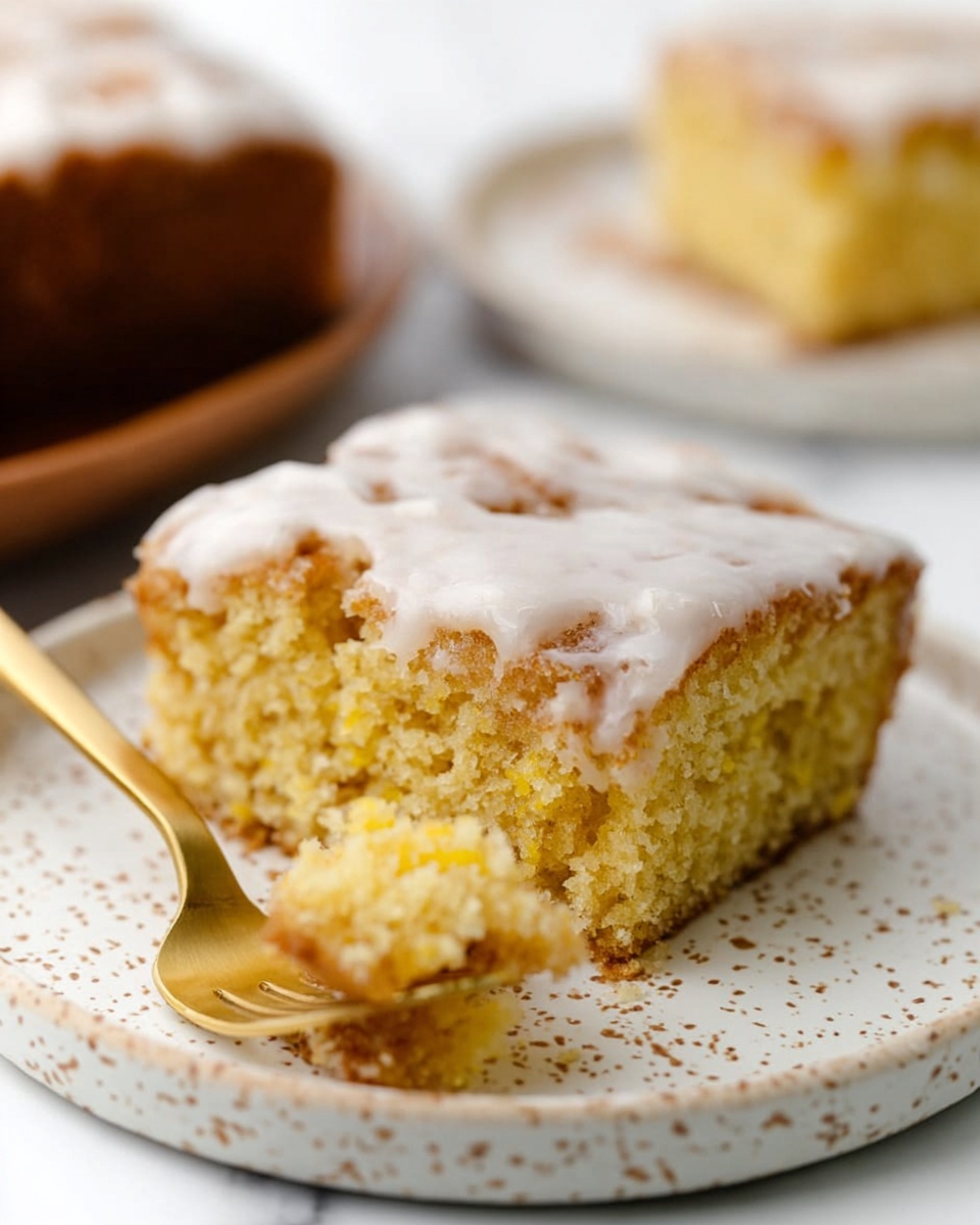 A close-up of a square slice of yellow cake with a crumbly texture, topped with a smooth, white glaze layer that looks slightly uneven and has small bubbly spots. The cake slice is on a white plate with small brown speckles, sitting on a white marbled surface. A gold fork holds a small bite of the cake in the front left side of the plate. In the background, another slice of the same cake is partially visible out of focus on a similar white speckled plate. Photo taken with an iphone --ar 4:5 --v 7