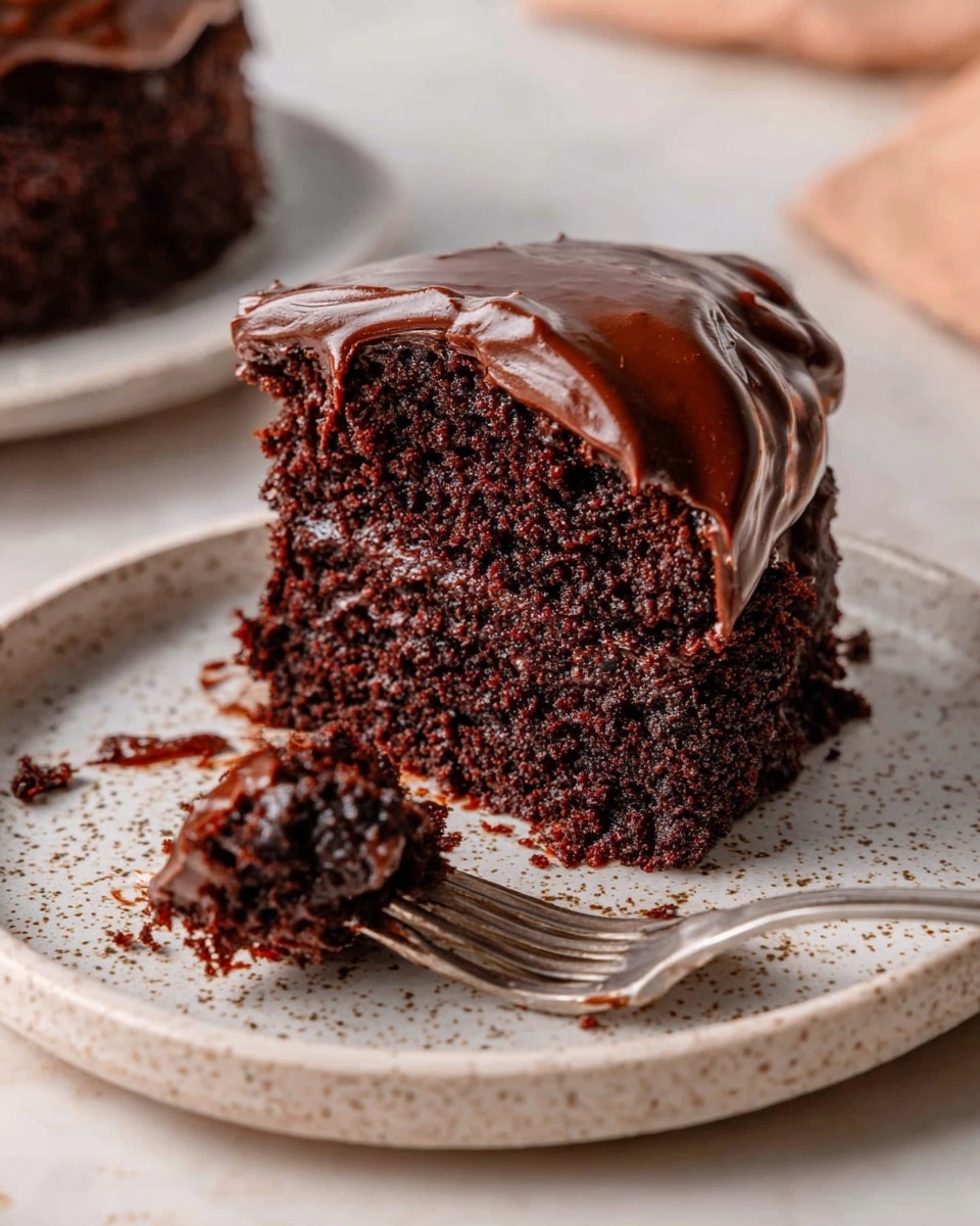 A close-up of a single slice of rich chocolate cake on a white speckled plate, showing two layers: a dense, moist dark brown cake base with a thick, smooth, and glossy dark chocolate frosting layer spread on top, slightly dripping off the side. A silver fork rests on the plate with some cake crumbs and frosting stuck to its tines, and a small piece of cake is on the fork. The background is a white marbled surface with subtle warm tones. photo taken with an iphone --ar 4:5 --v 7