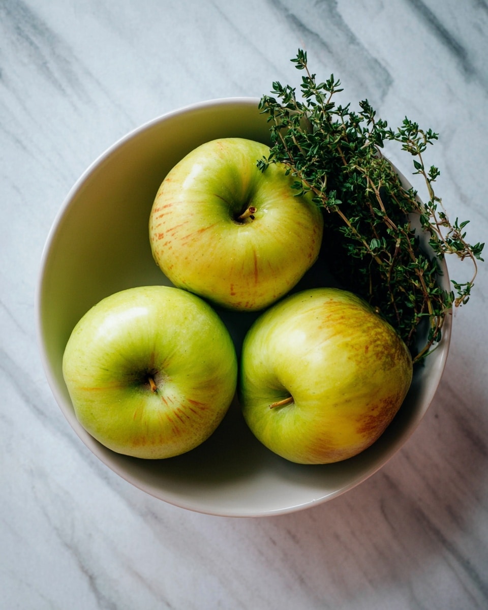 A simple white bowl holds four green apples with a slight yellow and red tint, arranged closely together, three forming a rough triangle with one placed in the middle at the bottom. On the right edge of the bowl, a small bunch of green fresh herbs adds a touch of deep green to the scene. The bowl is set on a white marbled surface that contrasts with the vibrant colors of the apples and herbs. photo taken with an iphone --ar 4:5 --v 7