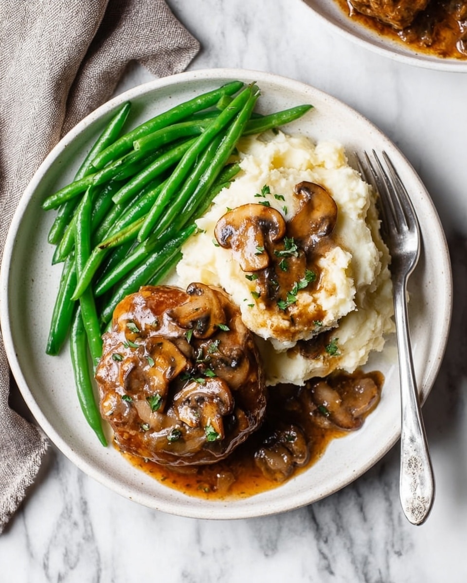 A round white plate on a white marbled background holds a meal with three main parts. On the left side are bright green, whole green beans with a smooth, fresh texture. In the center front, there is a small, thick, oval-shaped piece of meat covered with a dark brown mushroom sauce that includes sliced mushrooms and small bits of herbs. On the right side is a large scoop of creamy mashed potatoes with a soft, slightly lumpy texture, topped with more mushroom sauce and a few mushrooms. A silver fork is placed on the right edge of the plate, resting on the mashed potatoes. The photo was taken with an iphone --ar 4:5 --v 7