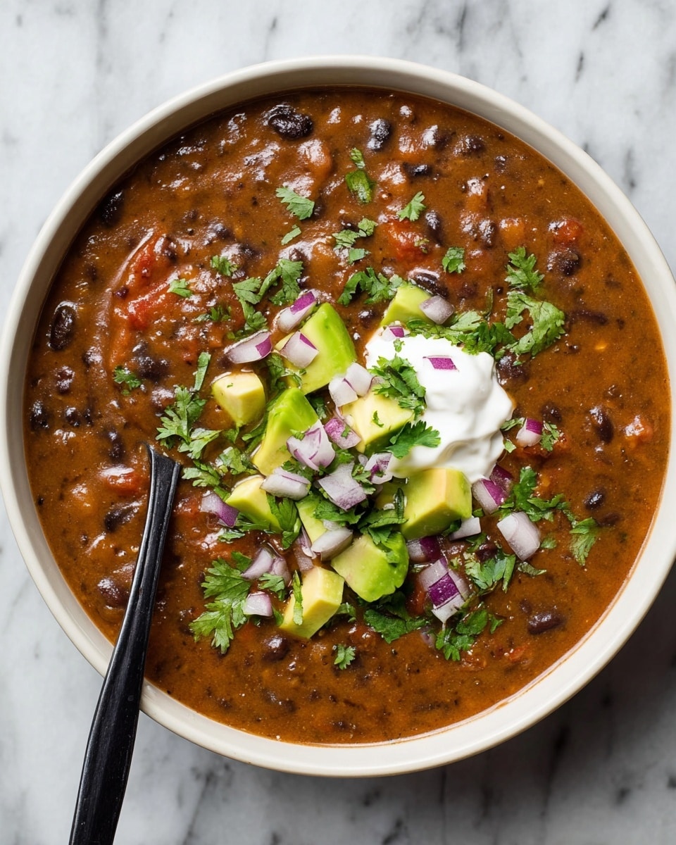 A bowl filled with thick black bean soup, warm brown with some black beans and small bits of tomatoes visible in the texture. The soup has a dollop of white sour cream near the center, topped with bright green avocado cubes, chopped fresh cilantro leaves, and small pieces of purple onion scattered evenly on top. A black spoon is dipped slightly into the soup on the left side, showing the thick texture. The bowl is white and placed on a white marbled surface. photo taken with an iphone --ar 4:5 --v 7