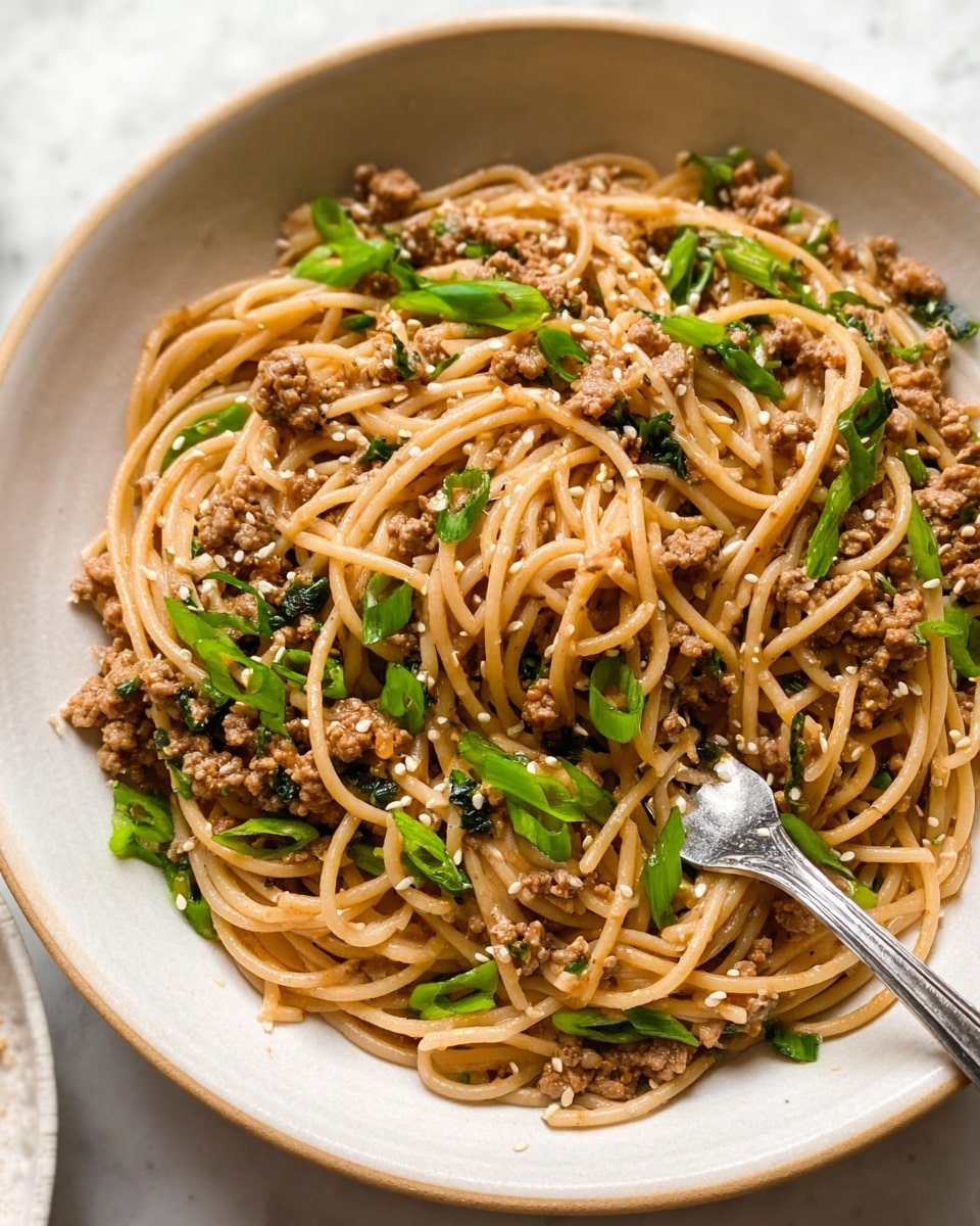 A white bowl filled with a mix of light brown spaghetti noodles and small bits of cooked minced meat, evenly spread throughout. Scattered on top are bright green sliced spring onions and small white sesame seeds, adding texture and color contrast. The noodles have a slightly glossy look, hinting at a light sauce coating. A silver fork is tucked into the right side of the bowl, with its prongs partially immersed in the noodles. The bowl sits on a white marbled surface, adding a clean and bright background. photo taken with an iphone --ar 4:5 --v 7