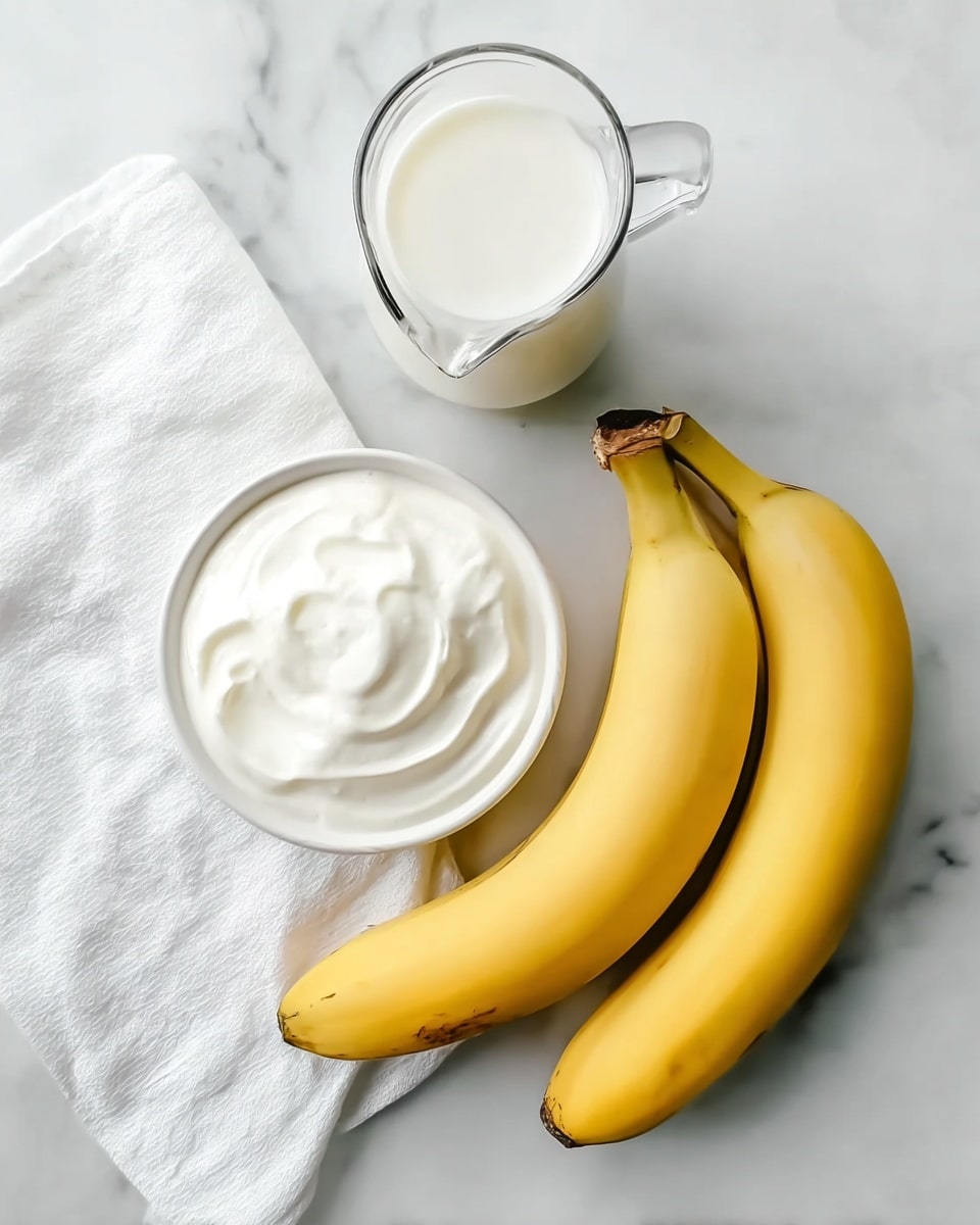 The image shows two bright yellow bananas placed side by side on a white marbled surface. Above the bananas, there is a white jug filled with milk, showing a smooth and shiny texture. Below the bananas, a small white bowl holds a thick, creamy white yogurt with soft peaks. A white cloth napkin is visible on the left side of the image partly under the bananas. The clean arrangement has a fresh, simple look. Photo taken with an iphone --ar 4:5 --v 7