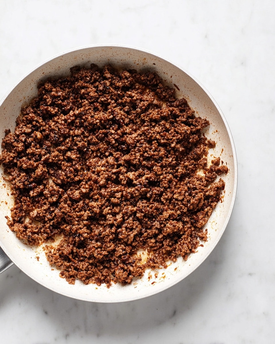A white pan filled with cooked ground meat that is broken into small uneven pieces, showing a rich brown color with some darker crispy parts, spread evenly across the pan's surface. The white pan contrasts with the dark brown cooked meat, sitting on a white marbled surface. There is no other visible layer or ingredient in the pan photo taken with an iphone --ar 4:5 --v 7