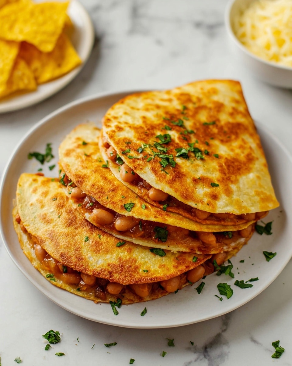 Three golden-brown quesadillas filled with light brown beans are stacked slightly overlapping on a white plate. The quesadillas have a crispy texture with some browned spots, and are sprinkled on top with small, fresh green herb pieces. Around the plate, more herbs are scattered on a white marbled surface. In the background, there are two yellow tortilla chips and part of a white plate with some shredded cheese. photo taken with an iphone --ar 4:5 --v 7