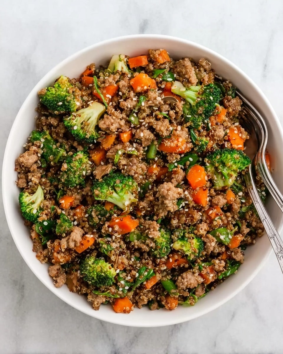 A white bowl filled with a colorful mixture of cooked quinoa, bright green broccoli florets, small orange carrot pieces, and browned ground meat mixed evenly throughout. There are small bits of green spinach leaves scattered in the dish, and white sesame seeds sprinkled on top. Two metal forks rest inside the bowl on the right side. The bowl sits on a white marbled surface. photo taken with an iphone --ar 4:5 --v 7