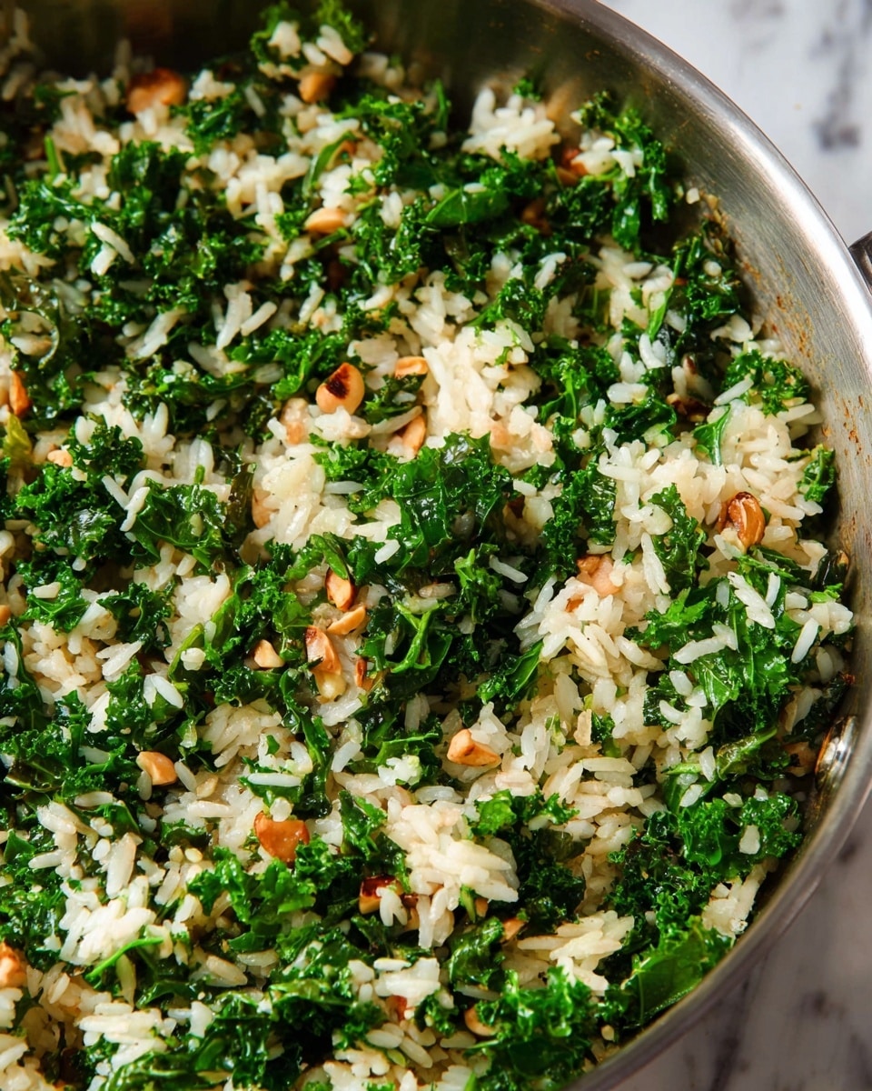 A close-up view of a cooked rice dish mixed with kale and small pieces of nuts in a metal pan. The dish has three main layers visible in the mix: the fluffy white rice grains, bright green curly kale leaves, and light brown nuts scattered evenly. The colors are natural and fresh, with the green kale standing out against the white rice and light brown nuts. The pan is shiny silver, and the background shows a white marbled texture. Photo taken with an iphone --ar 4:5 --v 7