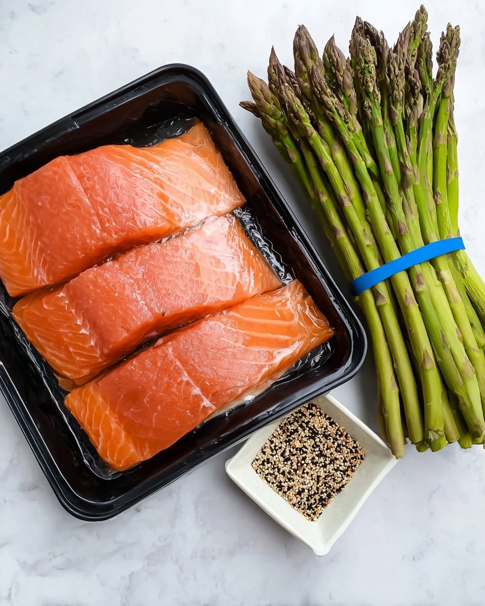 The image shows a black plastic tray filled with three pieces of fresh salmon fillets placed one on top of the other, displaying a smooth, shiny orange surface with white lines of fat. To the right, there is a large bundle of green asparagus stalks held together with two blue rubber bands, showing pointed tips and firm texture. Below the salmon tray, there is a small white square bowl containing a mix of black, white, and golden seasoning seeds. The items are all placed on a white marbled surface. Photo taken with an iphone --ar 4:5 --v 7