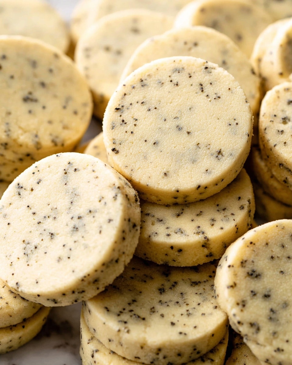 The image shows many round shortbread cookies stacked closely. Each cookie has a pale yellow color with small black specks evenly spread throughout the surface, giving a speckled effect. The cookies have a smooth and slightly grainy texture, with soft edges that are slightly thicker at the sides, indicating thickness about one layer each. The background is a white marbled texture, softly out of focus, making the cookies stand out clearly. photo taken with an iphone --ar 4:5 --v 7