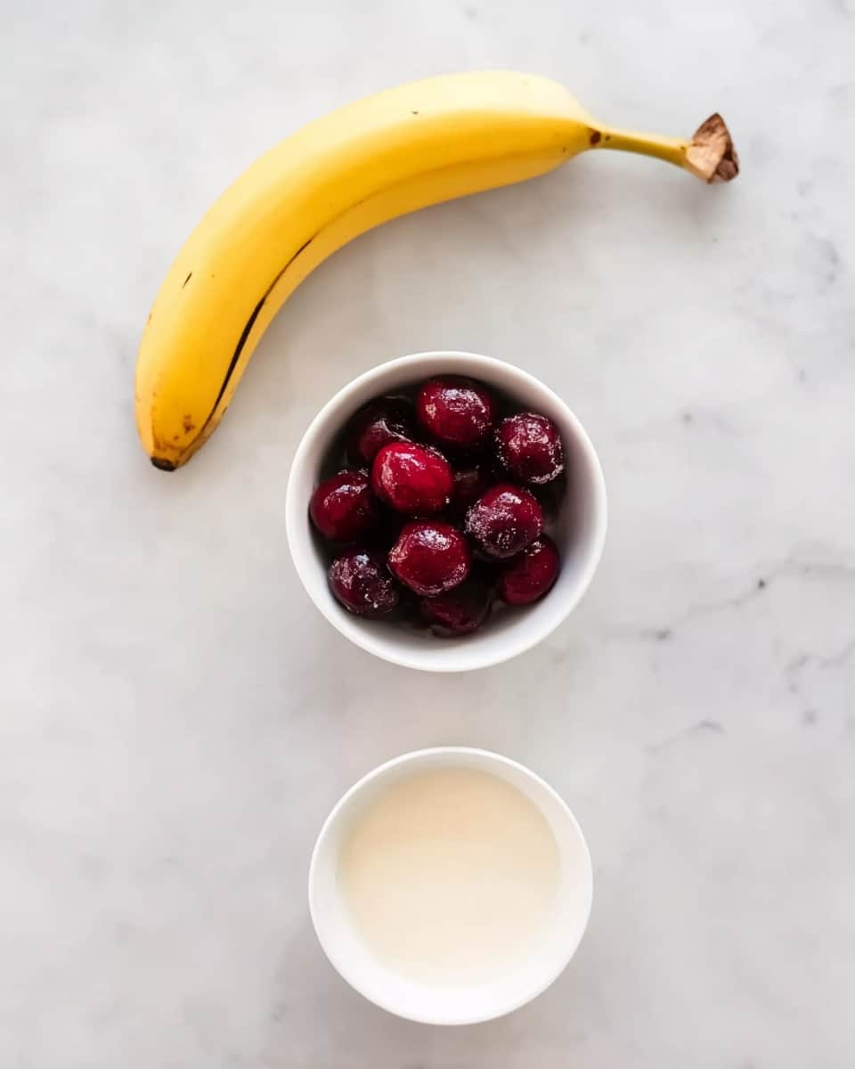The image shows three items placed on a white marbled surface arranged vertically. At the top, there is a yellow banana with a slightly dark tip on the left stem. In the middle, there is a small white bowl filled with dark red frozen cherries. At the bottom, there is another small white bowl filled with a creamy white liquid. The background is clean and bright, highlighting the colors of the fruit and liquid. Photo taken with an iphone --ar 4:5 --v 7