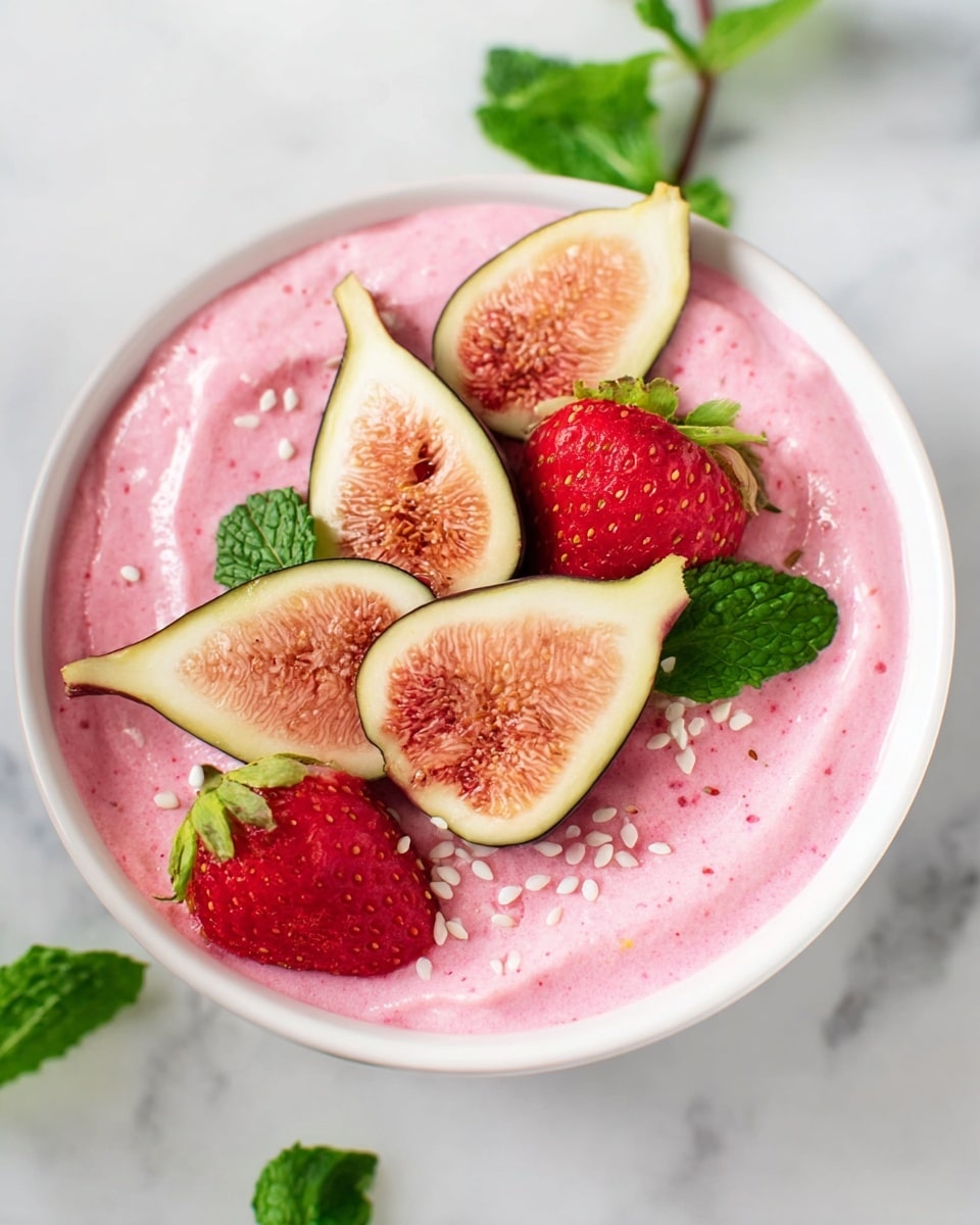 A white bowl filled with one smooth, creamy layer of bright pink yogurt or smoothie. On top, there are five fruit pieces arranged in a circle: three light pinkish-beige fig slices with greenish edges, and two red strawberry halves with green tops. Small white seeds sprinkle over the fruit and smoothie. A white marbled surface is under the bowl with some mint leaves visible nearby photo taken with an iphone --ar 4:5 --v 7