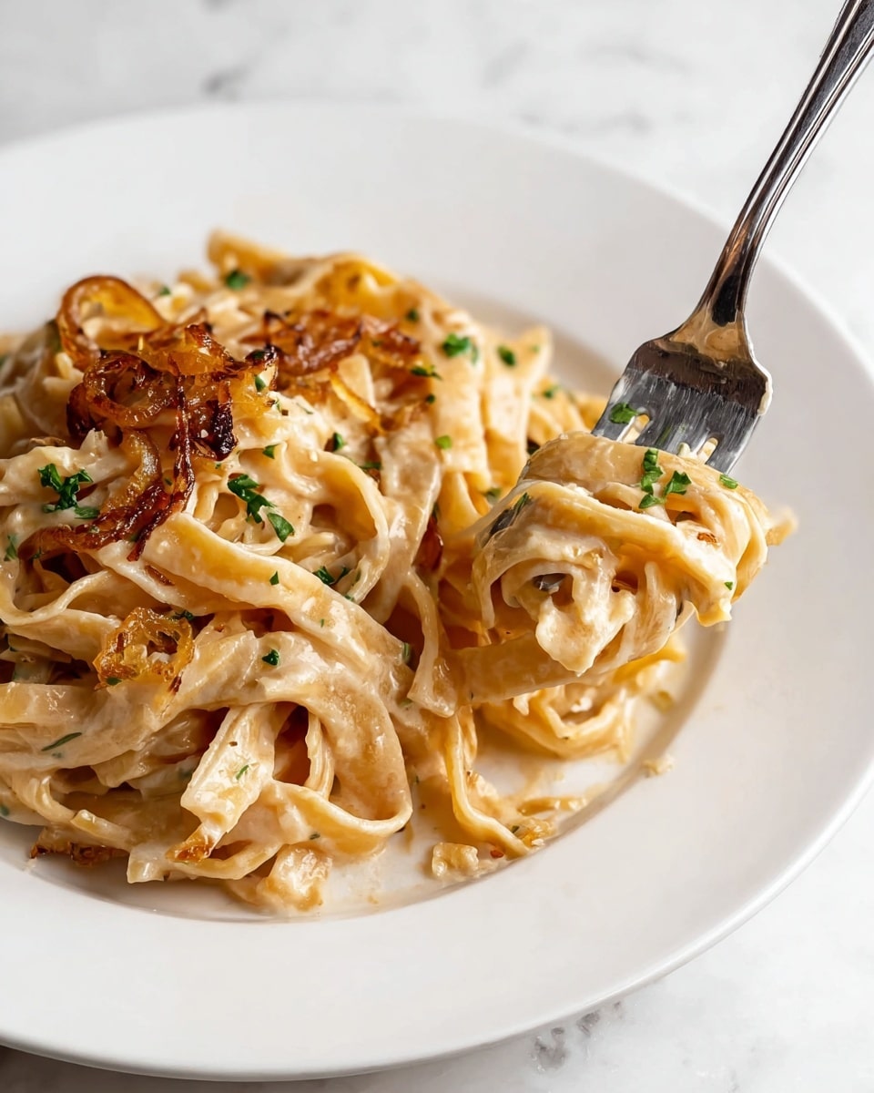 A close-up view of a white plate holding creamy pasta with about two layers of thick, flat noodles, each coated in a light beige sauce with a smooth texture. On top and mixed inside are golden-brown cooked onion strips adding crunch and color contrast, along with small green herb leaves scattered across for a fresh look. A silver fork lifts a small bundle of pasta from the right side of the plate, with the pasta strands swirling around its tines. The plate sits on a white marbled surface. Photo taken with an iphone --ar 4:5 --v 7