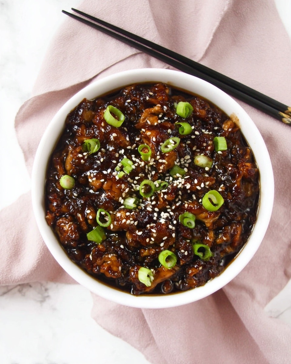 A white bowl filled with a dark brown, glossy cooked mixture that looks sticky with small chunks, topped with scattered white sesame seeds and bright green sliced scallions, sitting on a light pink cloth with black chopsticks placed above the bowl on a white marbled surface photo taken with an iphone --ar 4:5 --v 7