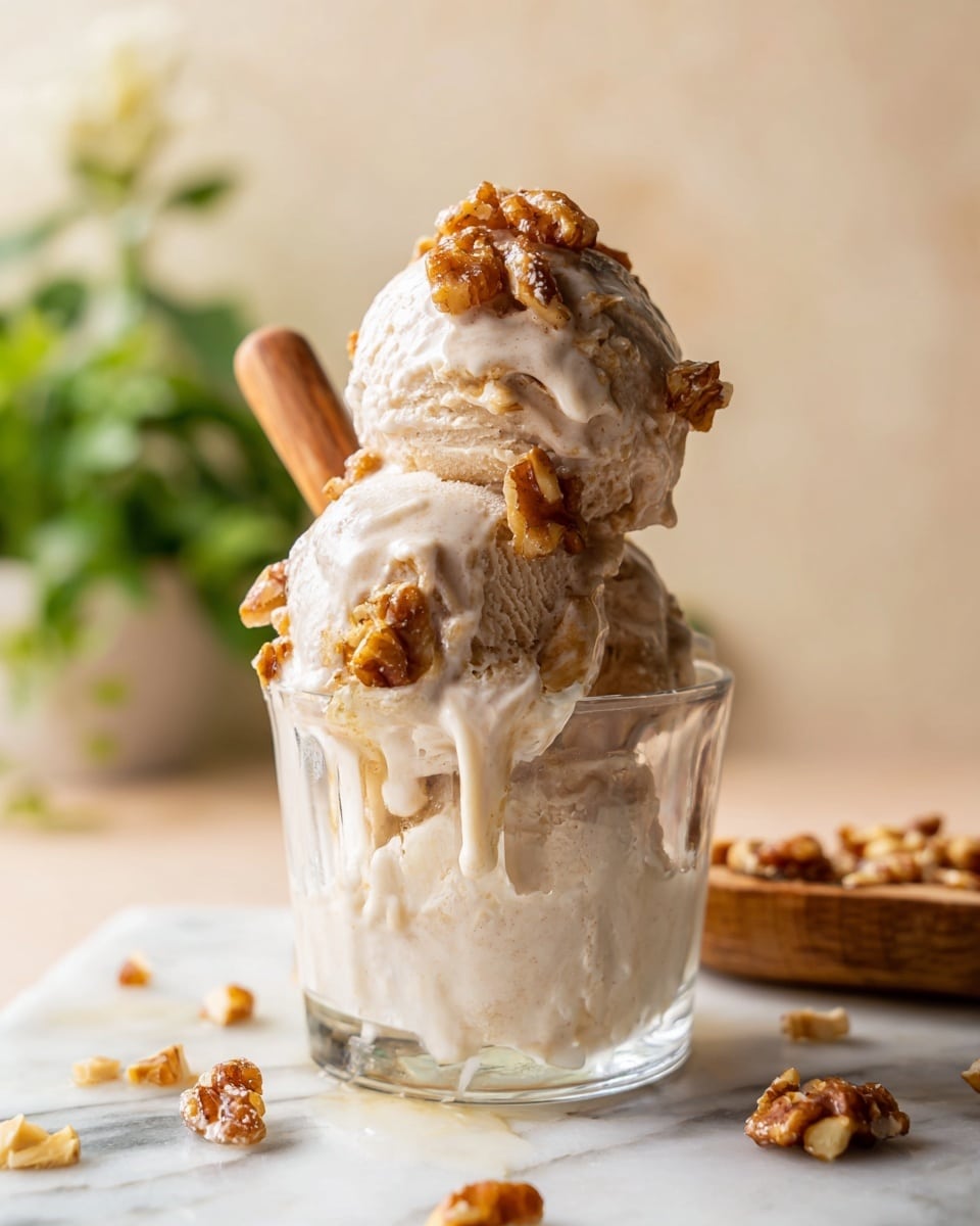 A close-up view of three scoops of light beige ice cream stacked in a clear glass, with the ice cream melting and dripping down the sides. On top and around the ice cream are chunky pieces of toasted brown nuts, adding texture and contrast. The glass sits on a white marbled surface with scattered nut pieces. In the softly blurred background, pale cream and green plant colors are visible, enhancing the warm and natural look. Photo taken with an iphone --ar 4:5 --v 7