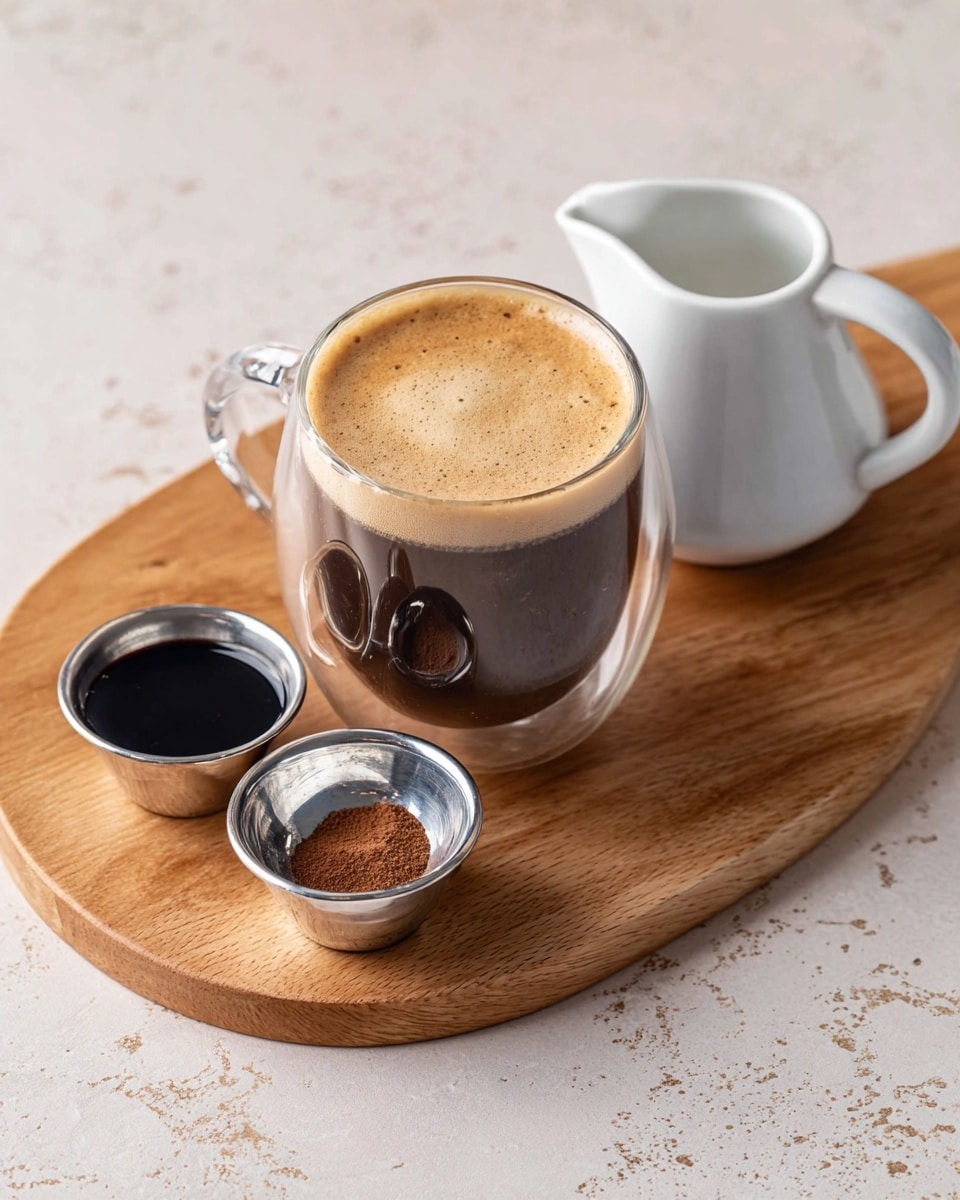 A clear glass with a dark brown coffee topped with light brown foam sits on a light wooden board with a small white jug on the right and two small silver bowls in front, one filled with dark syrup and the other with a small amount of brown powder, all placed on a white marbled surface photo taken with an iphone --ar 4:5 --v 7