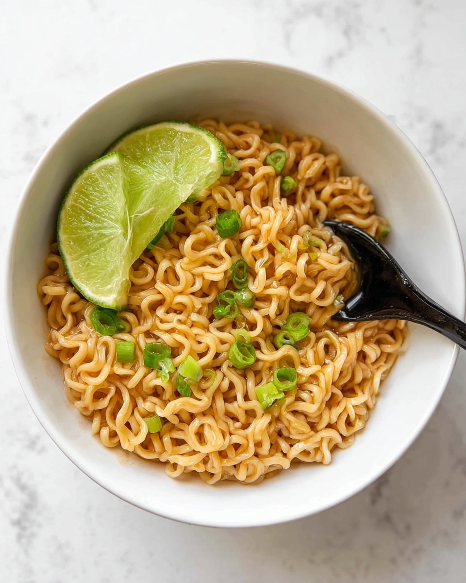 A white bowl filled with light brown curly noodles forms the main layer, slightly glossy and soft in texture. On top of the noodles, there are small bright green chopped scallions scattered evenly. Two large green lime wedges rest on the left inner side of the bowl, adding a fresh look. A black spoon is tucked into the noodles on the right, lifting some noodles with its glossy surface reflecting light. The bowl is placed on a white marbled surface. Photo taken with an iphone --ar 4:5 --v 7