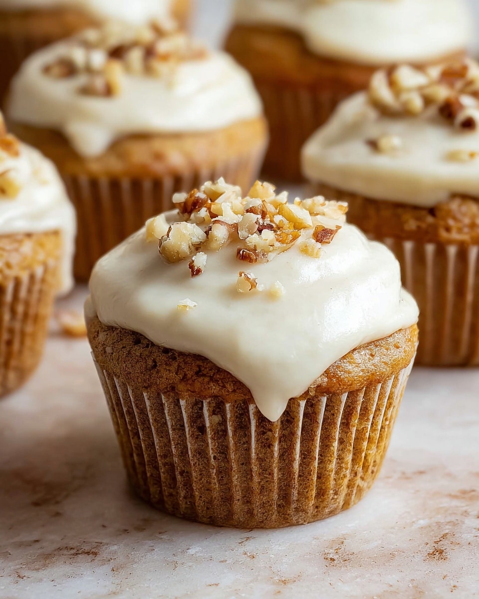 The image shows several light brown cupcakes with soft, slightly textured tops, each covered with a thick layer of smooth, creamy white frosting that spreads over the top edge and drips slightly down the sides. On top of the frosting, there are small clusters of chopped nuts lightly scattered, adding a rough texture and a hint of color contrast. The cupcakes sit on a light beige surface with a subtle white marbled texture, arranged close together with one cupcake in clear focus in the front and others slightly blurred in the background. photo taken with an iphone --ar 4:5 --v 7