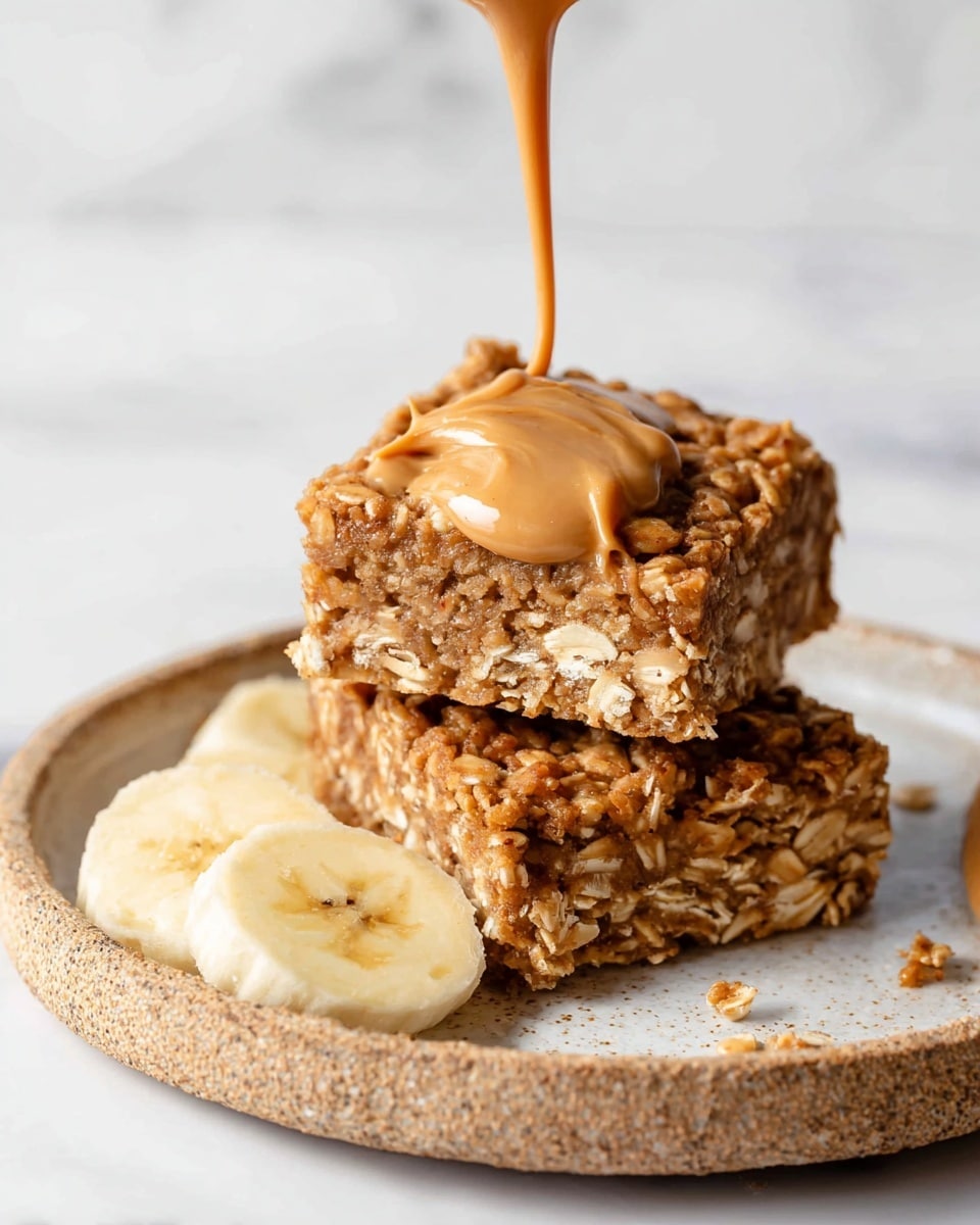 The image shows two square oat bars stacked on a round white plate with a rough texture. The bars have a brown, crumbly, and slightly textured look, with visible oats and small bits of banana inside. On top of the upper bar, thick peanut butter is being poured slowly, creating a smooth, creamy golden-brown layer. To the side of the plate, there are a few slices of fresh banana. The background is a white marbled texture. Photo taken with an iphone --ar 4:5 --v 7